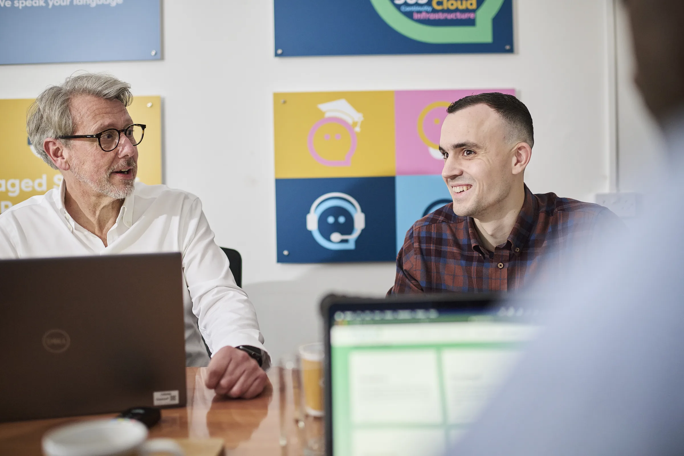 Two members of the Osiris IT team talking in the Norwich office, with the company's service artwork on the wall behind them.
